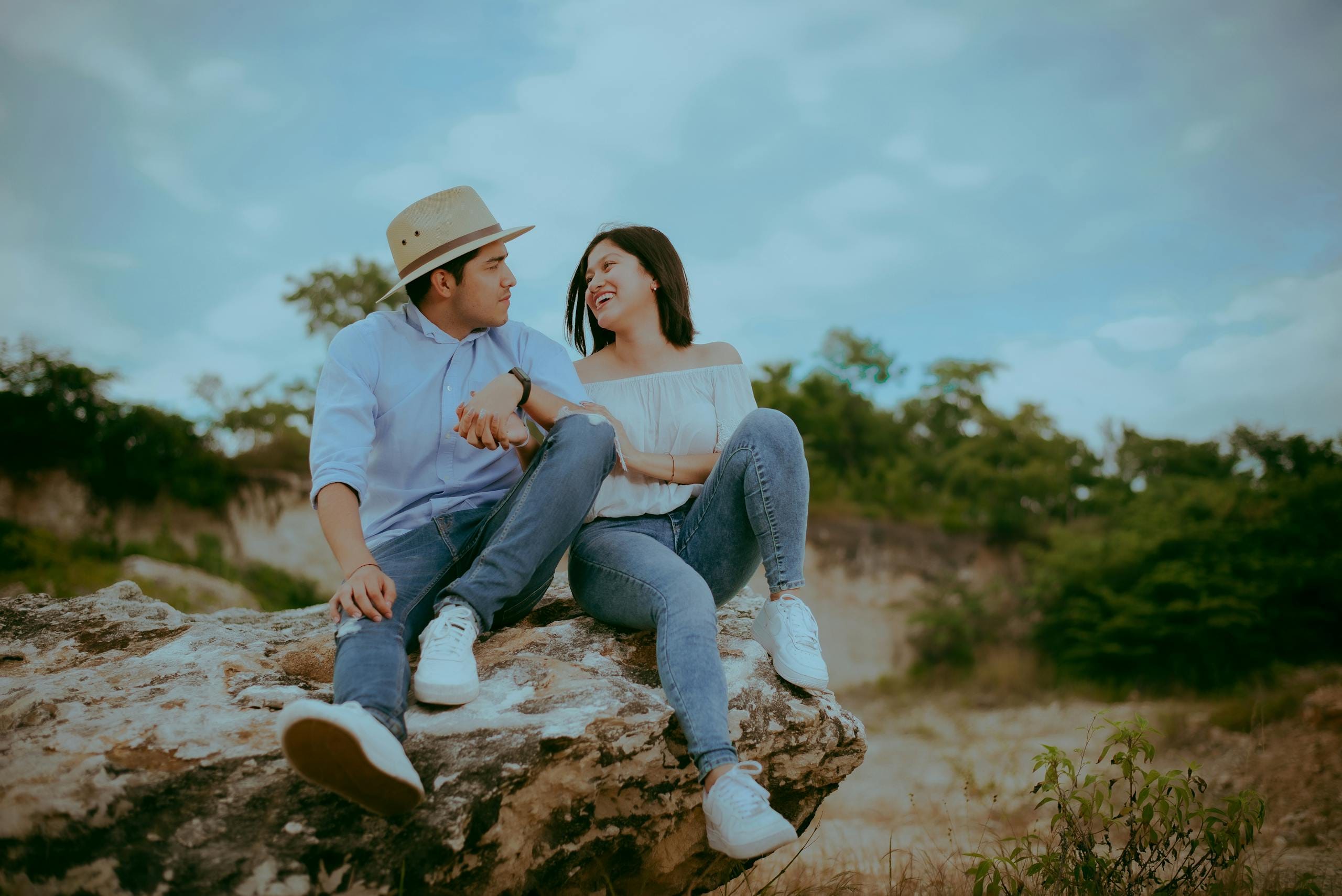 A happy couple sitting on a rock, sharing a joyful moment outdoors in nature.