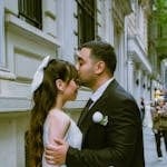 Bride and groom share a romantic kiss outdoors on a cobblestone street, capturing the essence of love and marriage.